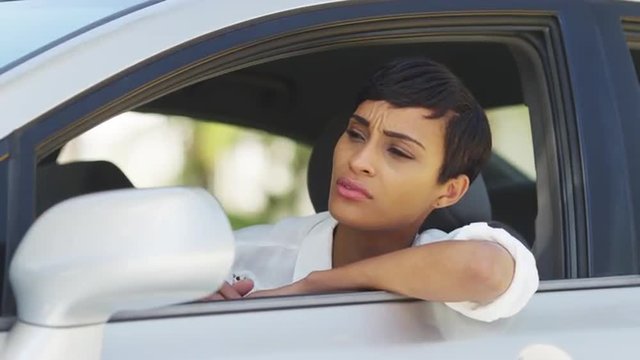 African woman in car looking around and checking hair in mirror