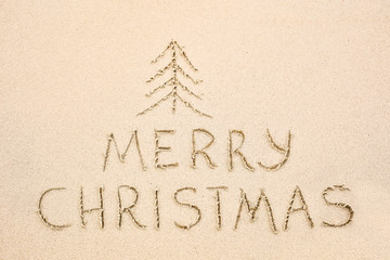 Merry Christmas inscription on wet yellow beach sand