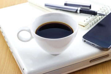 Fototapeta na wymiar Coffee cup on laptop and mobile or pen with notepad for business