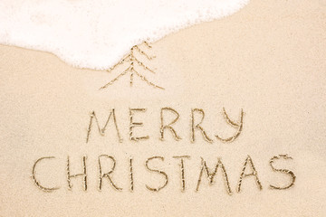 Merry Christmas inscription on wet yellow beach sand