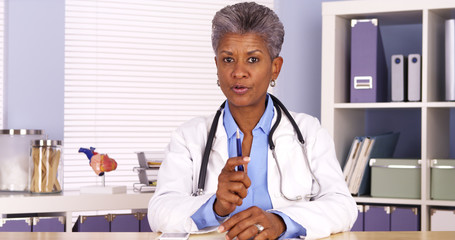 Senior african doctor sitting at desk and talking to camera