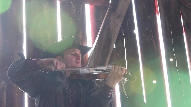 A cowboy playing a smoking fiddle in a cool old barn