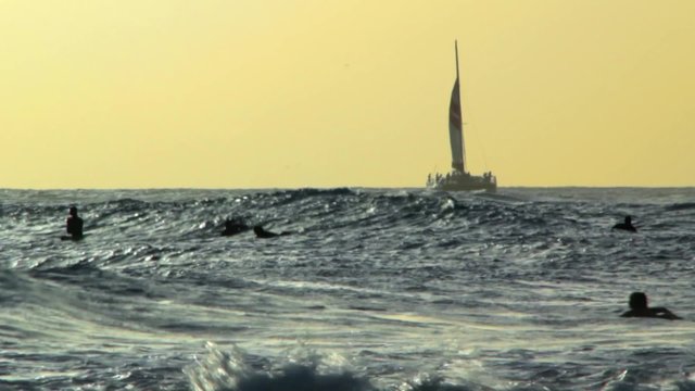 Sufers catching a wave and sailboat