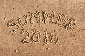 Fototapeta premium Summer 2016 written on the sand in the rays of the sun