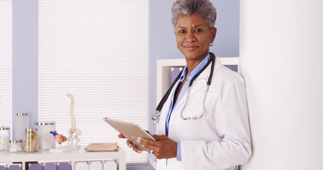 Serious Black Senior doctor working on tablet in office