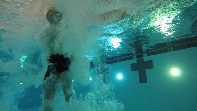 Slow motion of a boy jumping into pool underwater shot