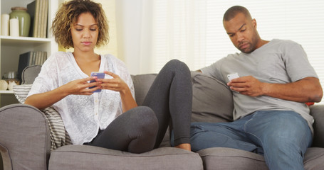 Black couple using smartphones on couch