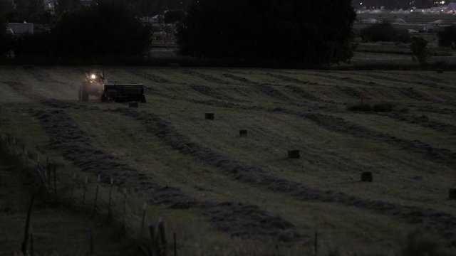 A farmer bailing hay at evening