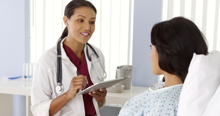 Obraz premium Female African doctor talking to Hispanic patient using tablet computer