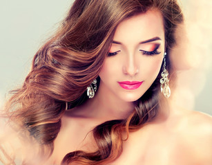 Beautiful model brunette with long curled hair and jewelry earrings