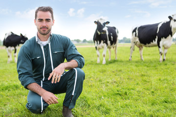 Portrait of a young attractive farmer in a pasture with cows