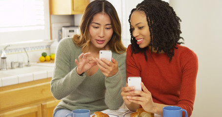 Two women best friends using smart phones and eating breakfast