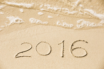 2016 inscription written in the wet yellow beach sand being wash