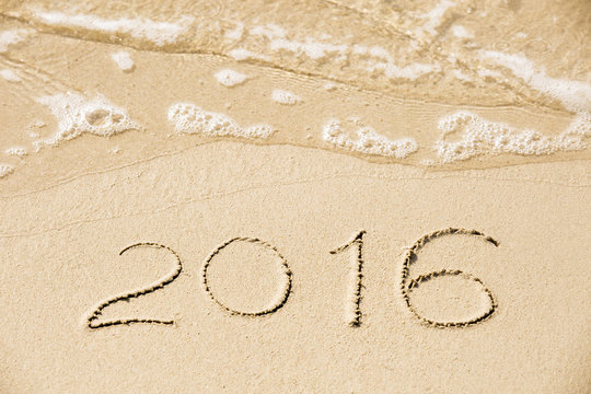 2016 inscription written in the wet yellow beach sand being wash