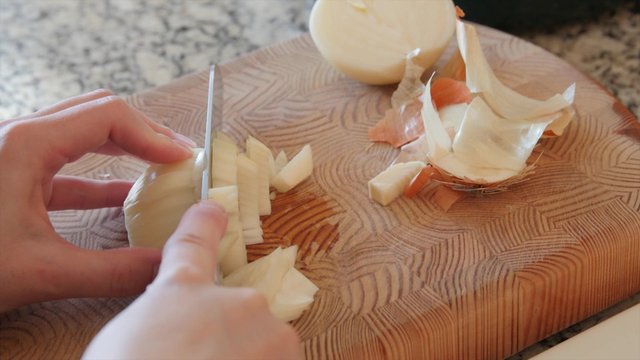 A woman dices an onion on a cutting board