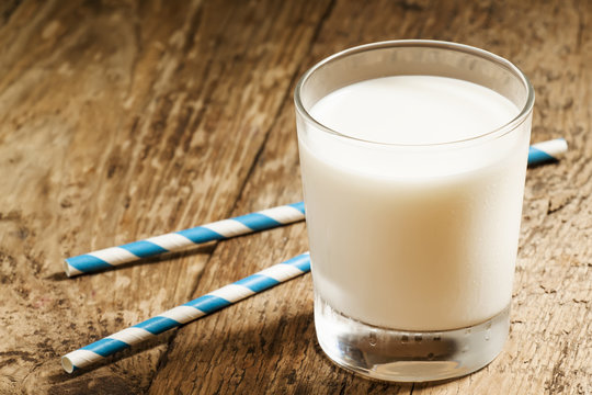 A glass of fresh milk with striped blue and white tubes on an ol