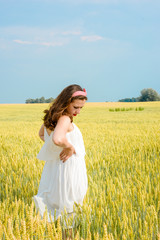 Fototapeta na wymiar A beautiful young woman on a wheat field. Stylish brunette girl with red lips standing in the field on a sunny day. Concept of freedom and happiness 