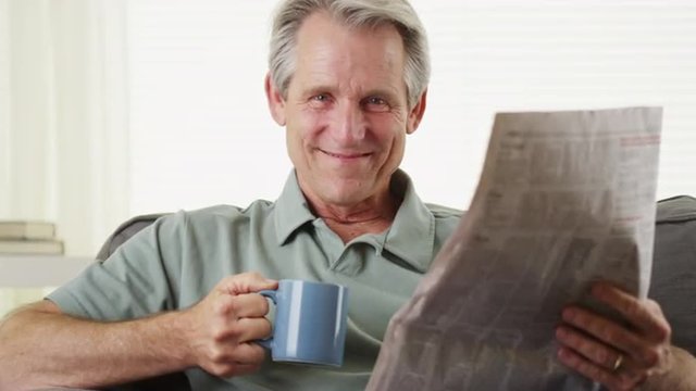 Smiling senior reading newspaper with coffee
