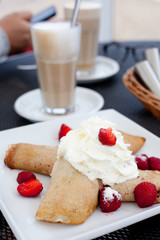 Crepes with berries and cream, latte on the background