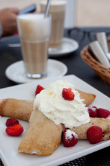 Crepes with berries and cream, latte on the background