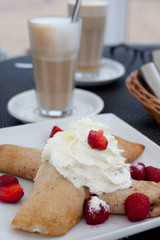 Crepes with berries and cream, latte on the background