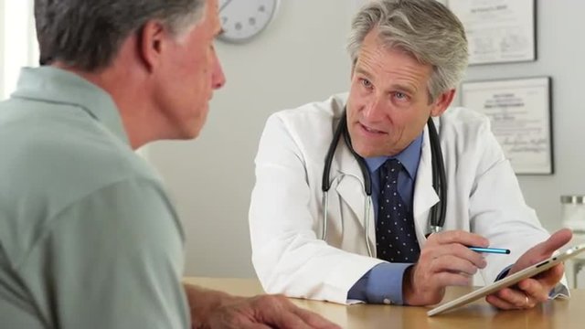 Mature doctor talking with patient and tablet in office