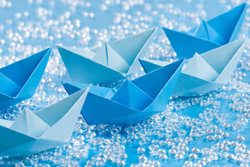 Fleet of blue Origami paper ships on blue waterlike background