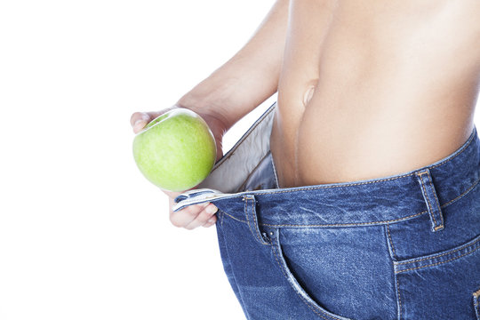 Mid section of slim woman wearing too big jeans holding an apple on white background
