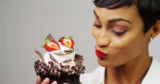 Black woman admiring a fancy dessert cupcake with chocolate and strawberries