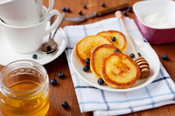 Fritters of cottage cheese with honey, sour cream and bilberry or blueberry on a white plate, delicious breakfast