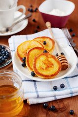 Fritters of cottage cheese with honey, sour cream and bilberry or blueberry on a white plate, delicious breakfast