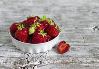 fresh strawberries in a white bowl on a light wooden background