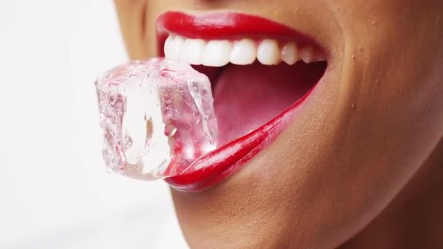 Close up of woman holding ice in mouth on white background