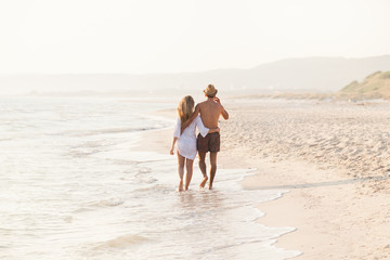 On a summer day a loving couple in swimsuit, walking embraced on the beach with no other people on the beach sand