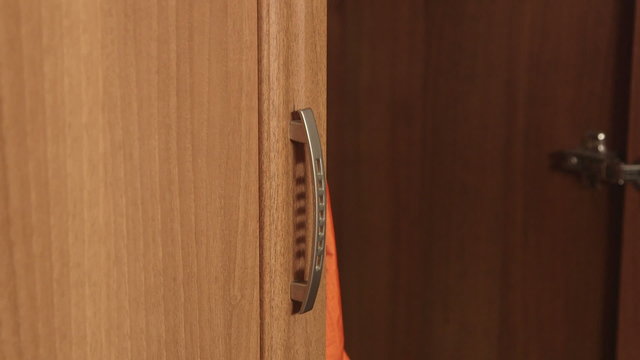 Female hand opening the closet door and pulling out raincoat close up