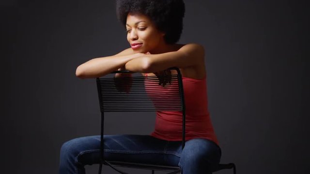 Smiling black woman sitting with arms over back of chair