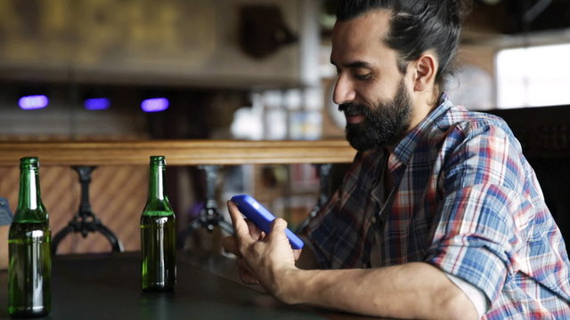 man with smartphone drinking beer at bar or pub