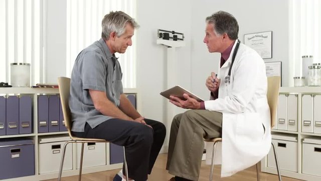 Senior doctor consulting mature patient with tablet