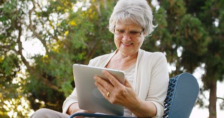 Senior woman happily surfing the web on tablet at the park