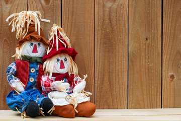 Two scarecrows sitting by wooden fence