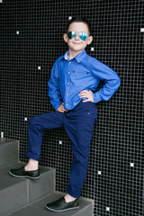 A cute little boy is dressed in a blue shirt and trousers. He we