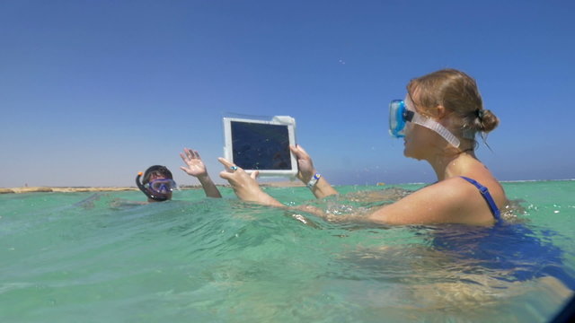 Woman and man in the sea making vacation photos with pad
