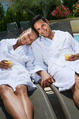 beautiful young couple resting in deck chairs with bathrobe by the pool of a thalasso resort - obrazy, fototapety, plakaty