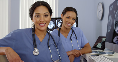 Smiling Hispanic and African American nurses sitting at computer station