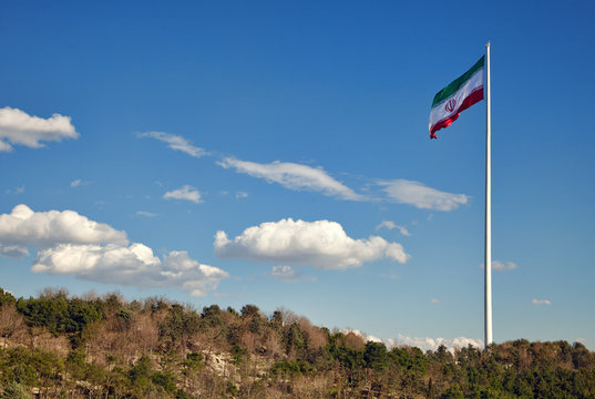 Large Iran Flag Waving in the Wind against Cloudy Blue Sky above Green Park Area in Tehran