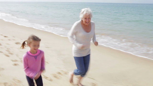 Grandmother And Granddaughter Running Along Beach Together