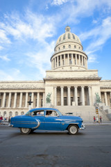 Classic blue American car passes in front of the Capitolio building in Central Havana