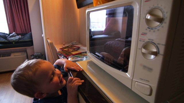 A family cooking frozen pizza in hotel microwave