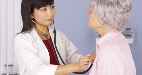 Asian doctor listening to elderly patient's heart