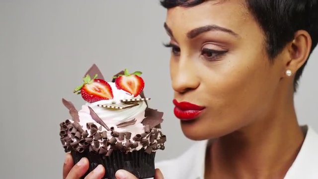 Black woman admiring a fancy dessert cupcake with chocolate and strawberries